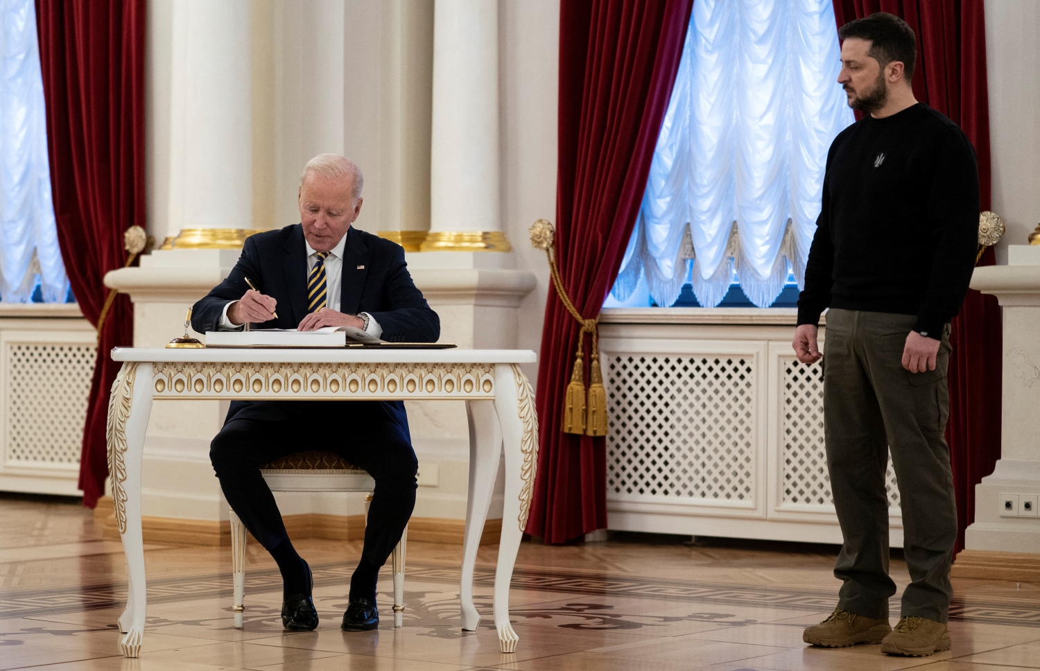 ފެބްރުއަރީ 20، 2023؛ އެމެރިކާގެ ރައީސް ޖޯ ބައިޑެން (ވ) ޔޫކްރޭނަށް ކުރެއްވި ސިއްރު ދަތުރުފުޅުގައި ޔޫކްރޭންގެ ވެރިރަށް ކިޔޭވްގައި ހުންނަ މަރިންސްކީ ގަނޑުވަރަށް ވަޑައިގެން، އިއްޒަތްތެރިން ސޮއި ކުރައްވާ ފޮތުގައި ސޮއި ކުރައްވާ އިރު، އަރިހުގައި ޔޫކްރޭންގެ ރައީސް ވޮލޮޑިމީރް ޒެލެންސްކީ. --އޭއެފްޕީ