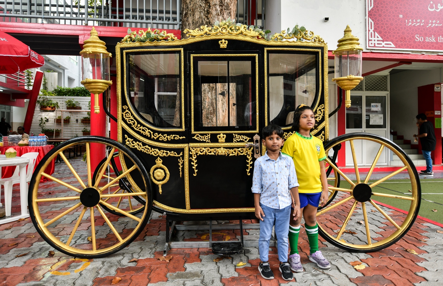 ފެއާއަށް ދިޔަ ކުދިންތަކެއް، ހޯލްގައި ބަހައްޓާފައިވާ ގާޑިޔަލެއްގެ ކައިރީގައި ފޮޓޯއަކަށް ހުއްޓިގެން -- ފޮޓޯ: ފަޔާޒް މޫސާ | މިހާރު