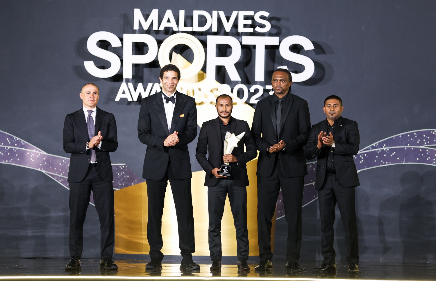 އެންމެ މޮޅު ފުޓްބޯޅަ ކުޅުންތެރިއަކަށް ހޮވި ގައުމީ ޓީމް އަދި މާޒިޔާގެ ކުޅުންތެރިޔާ ހަމްޒާ މުހައްމަދު (ހަމްޕް) އެވޯޑާއެކު ފޮޓޯއަކަށް ހުއްޓި ވަޑައިގެން: އަރިހުގައި ޔޫތު މިނިސްޓަރު އަހުމަދު މަހުލޫފާއި އާސެނަލްގެ ކުރީގެ ފޯވާޑް ންވަކްވޯ ކާނޫ އާ އިނގިރޭސި ގައުމީ ޓީމުގެ ކުރީގެ ގޯލްކީޕަރު ޑޭވިޑް ޖޭމްސް އަދި އިޓަލީގެ ލެޖެންޑް ފަބިއޯ ކަނަވާރޯ -- ފޮޓޯ: ފަޔާޒު މޫސާ | މިހާރު