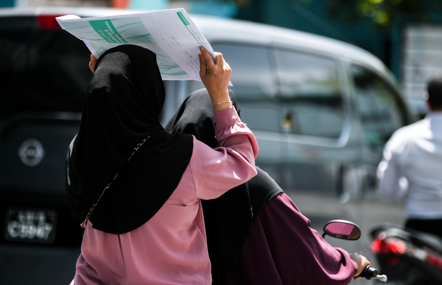 އައިޖީއެމްއެޗުން ނުކުމެގެން ދިޔަ ދެ މީހުންގެ ތެރެއިން ސައިކަލްގެ ފަހަތުގައި އިން މީހާ ހޫނު ގަދަވުމުގެ ސަބަބުން އެކްސްރޭ އެންވެލޮޕެއް ބޯ މަތީގައި އަޅައިގެން ދަނީ.--- ފޮޓޯ: ފަޔާޒު މޫސާ | މިހާރު