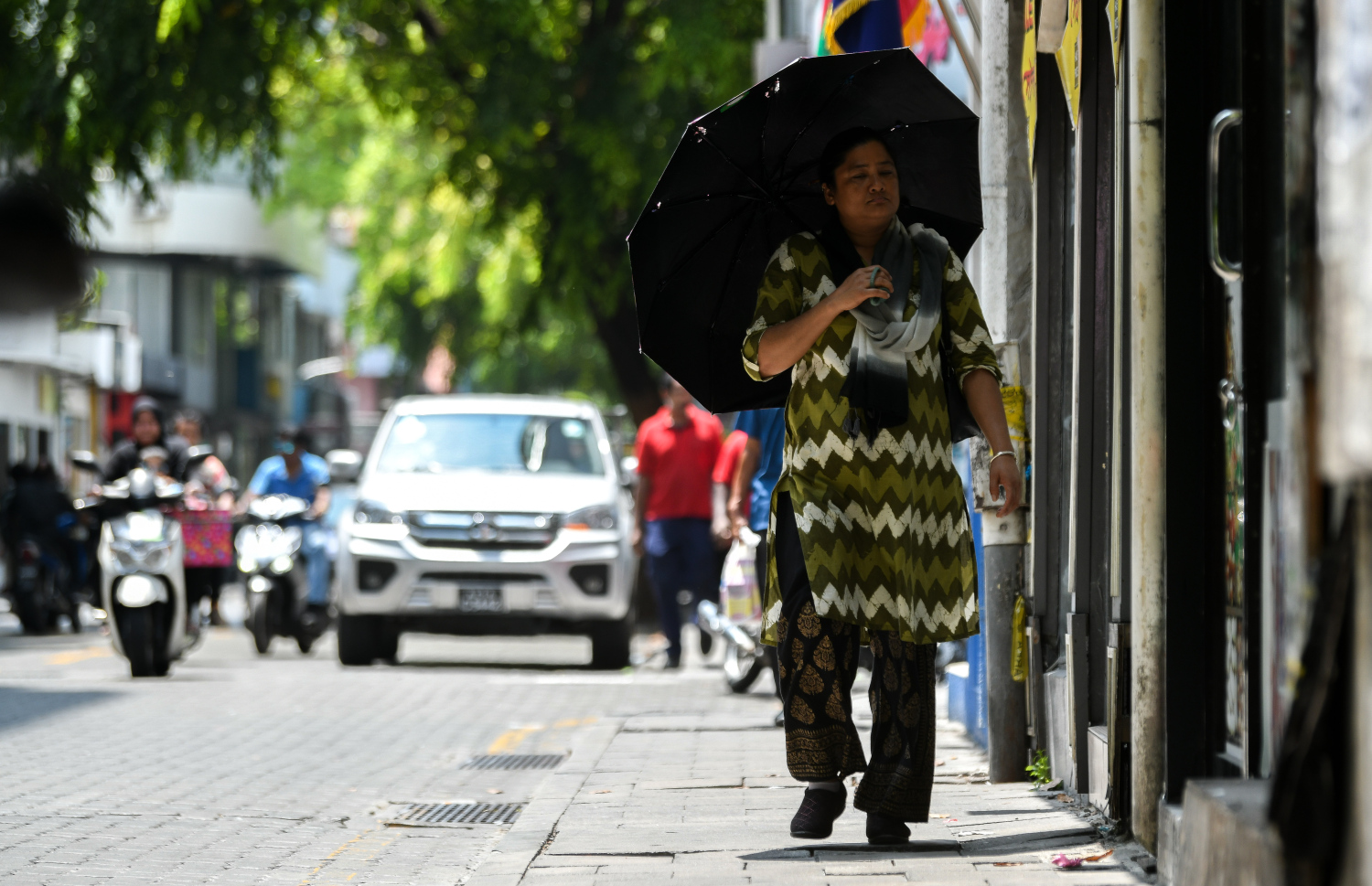 ހޫނުގަދަ ދުވަހެއްގައި މާލޭގެ މަގަކުން އަންހެނަކު އަވިން ސަލާމަތްވުމަށް ކުޑައެއް ނަގައިގެން ހިނގާފައި ދަނީ.-- ފޮޓޯ: ފަޔާޒް މޫސާ | މިހާރު