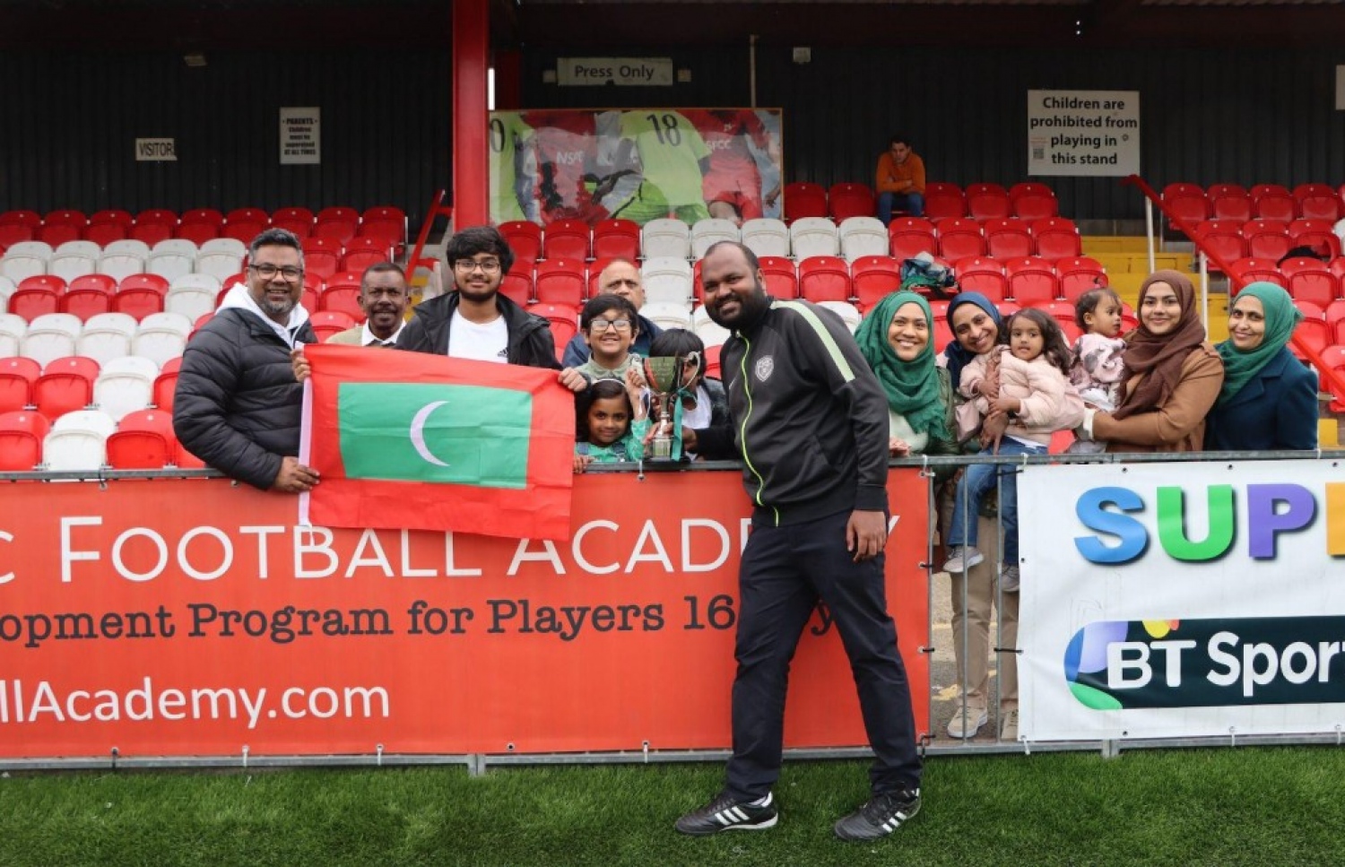 އަލީ ވަހީދު މުބާރާތުގެ ޗެމްޕިއަން ތަށި ހިފައިގެން، މެޗު ބަލަން ދިޔަ އިނގިރޭސިވިލާތުގައި ދިރިއުޅޭ ބައެއް ދިވެހިންނާ އެކު.-- ފޮޓޯ: ވަގުތު