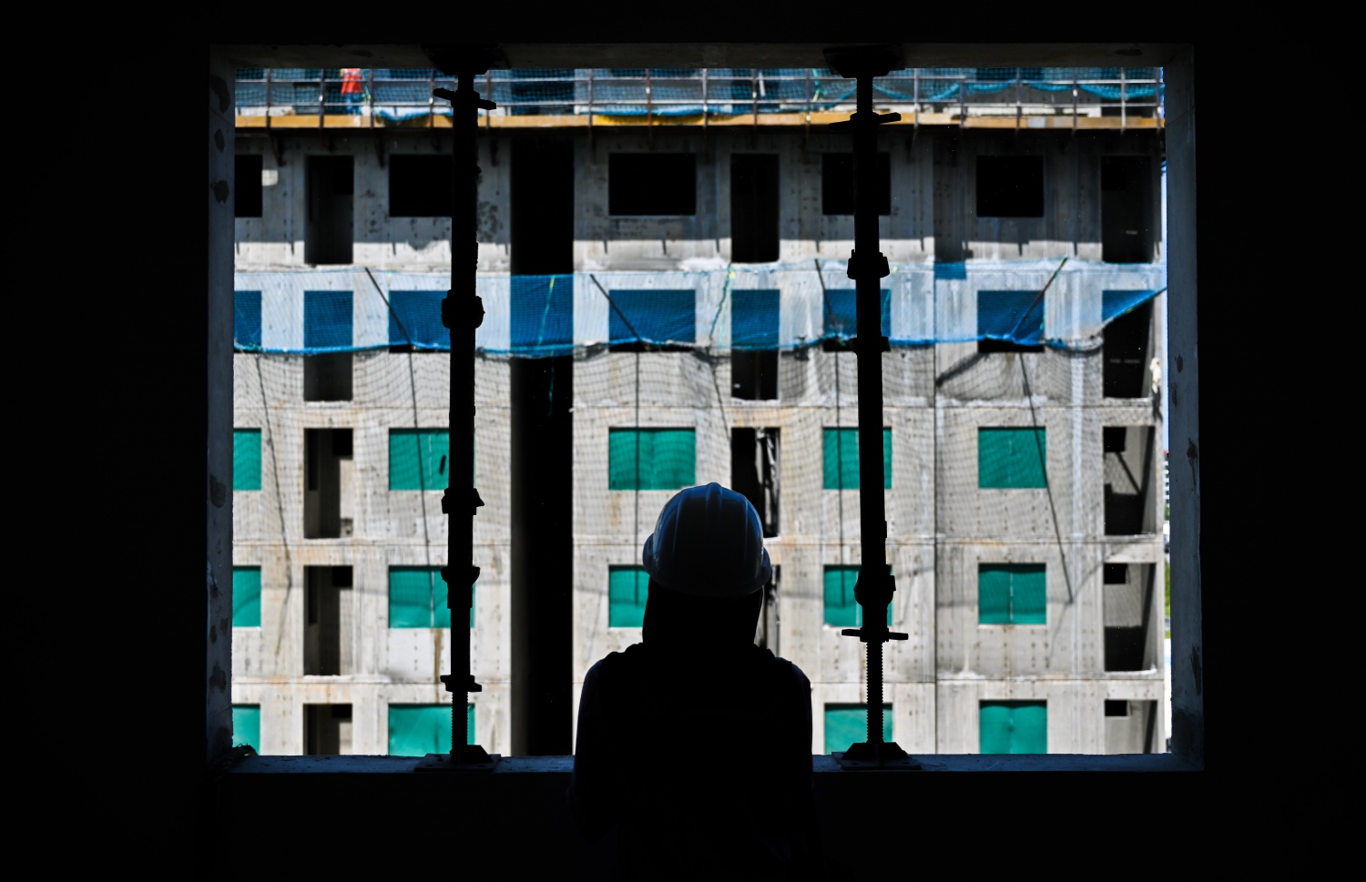 ހުޅުމާލެ 2 ގައި ހަދަމުން އަންނަ ފްލެޓެއްގެ ކުޑަދޮރުން ނޫސްވެރިޔަކު ބޭރު ބަލާލަނީ: މި ޕްރޮޖެކްޓްގައި މި އަހަރުގެ ނިޔަލަށް 8 ޓަވަރުގެ މަސައްކަތް ނިންމާލެވޭނެ.-- ފޮޓޯ: ފަޔާޒު މޫސާ | މިހާރު