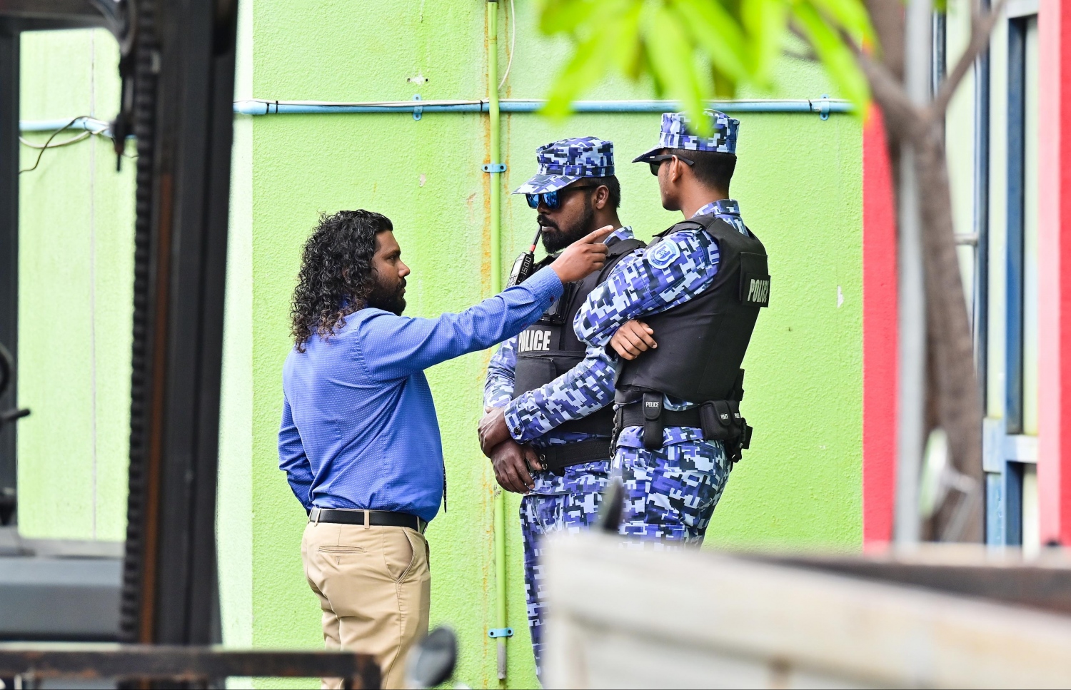 ފުލުހުން އެފްއޭއެމް ހައުސް އަށް ވަދެ ފާސްކުރާއިރު އެތަނުގެ ބޭރުގައި ތިބި ފުލުހުންގެ ބަޔަކާ މުވައްޒަފަކު ވާހަކަ ދައްކަނީ. -- ފޮޓޯ: ނިޝާން އަލީ/ މިހާރު