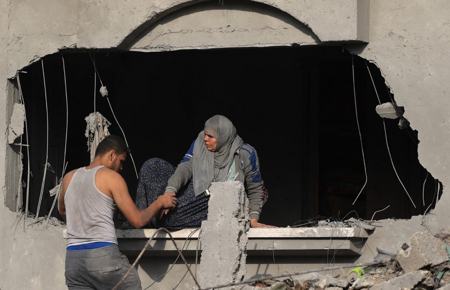 އިޒްރޭލުން ދިން ވައިގެ ހަމަލާއެއްގައި ހަލާކުވެފައިވާ ގެއަކުން، ފަލަސްތީނުގެ އަންހެނަކު ނުކުތުމަށް މީހަކު އެހީތެރިވަނީ.-- ފޮޓޯ: އޭއެފްޕީ