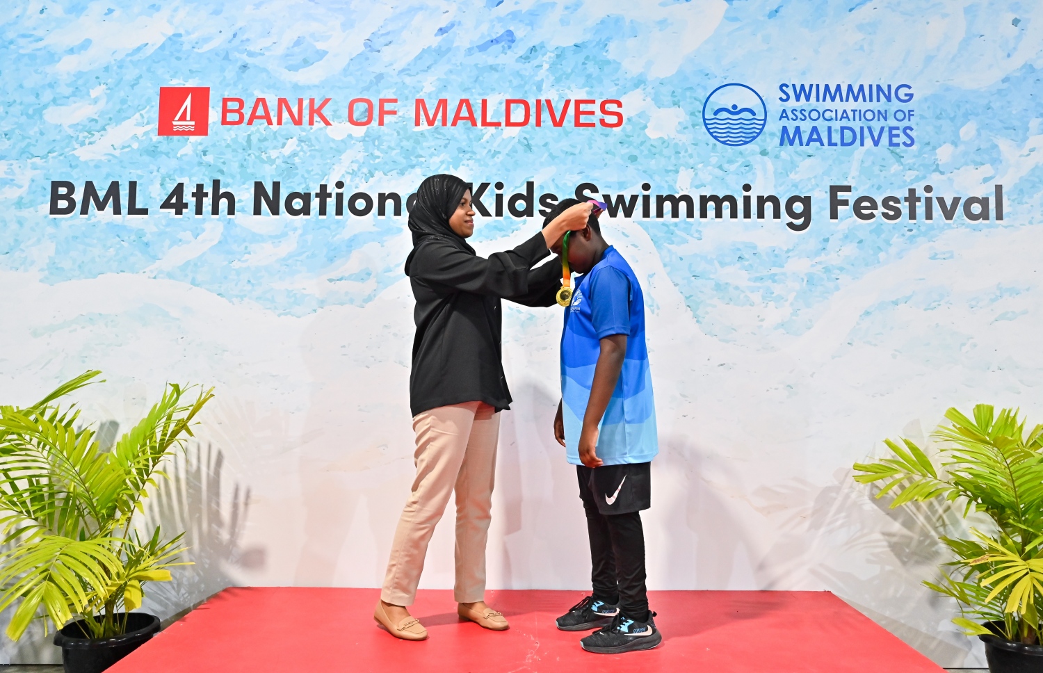 ބީއެމްއެލް ނެޝެނަލް ކިޑްސް ސްވިމިން ފެސްޓިވަލުގައި ބައިވެރިވި ފެތުރުންތެރިއަކާ މެޑަލް ހަވާލުކޮށްދެނީ.--- ފޮޓޯ: ފަޔާޒު މޫސާ | މިހާރު