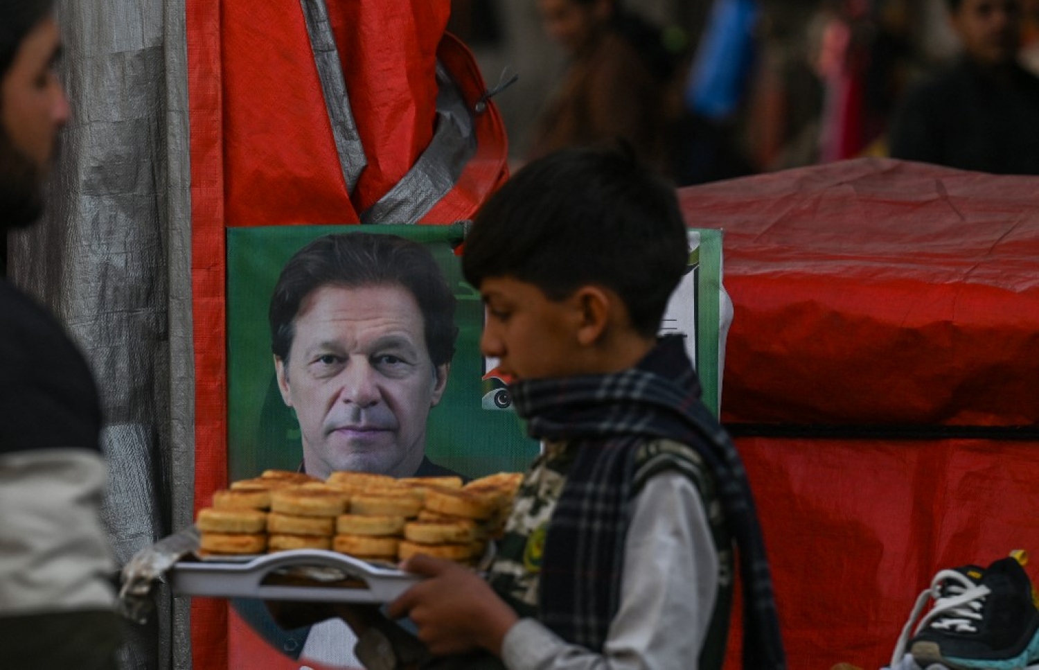 ޕާކިސްތާނުގެ ކުރީގެ ބޮޑުވަޒީރު އިމްރާން ޚާންގެ ފޮޓޯއެއް ކައިރިން، ކާތަކެތި އަޅާފައި ހުރި ތަބަކެއް ހިފައިގެން ކުއްޖަކު ހިނގާފައި ދަނީ. -- ފޮޓޯ: އޭއެފްޕީ