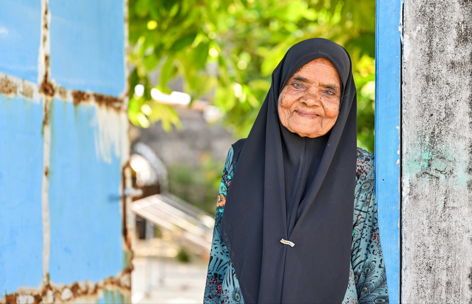 ށ. ޅައިމަގު، ރުގިއްޔާ އާދަމް އޭނާގެ ގޭގެ ދޮރުގައި ލެނގިލައިގެން ފޮޓޯއަކަށް ހުއްޓިގެން.-- ފޮޓޯ: ފަޔާޒް މޫސާ | މިހާރު