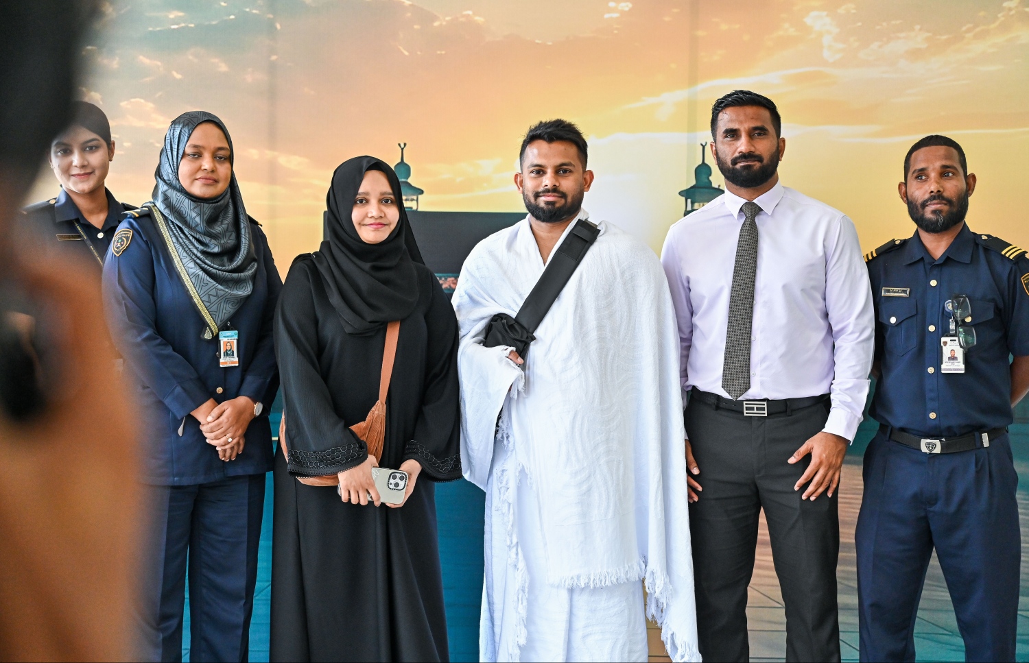 ރާއްޖެ އިން ހައްޖަށް ދާ މީހުންގެ ފަހު ގުރޫޕުގައި ހިމެނިވަޑައިގެންނެވި އިމިގްރޭޝަން ކޮންޓްރޯލަރު މުހައްމަދު ޝަމްއާން ވަހީދު ފުރާވަޑައިގަތުމުގެ ކުރިން، ޑެޕިއުޓީ އިމިގްރޭޝަން ކޮންޓްރޯލަރު އަޝްފާން އާއި ބައެއް އޮފިސަރުންތަކަކާ އެކު ފޮޓޯއެއް ނަންގަވަނީ.--- ފޮޓޯ: ފަޔާޒު މޫސާ | މިހާރު