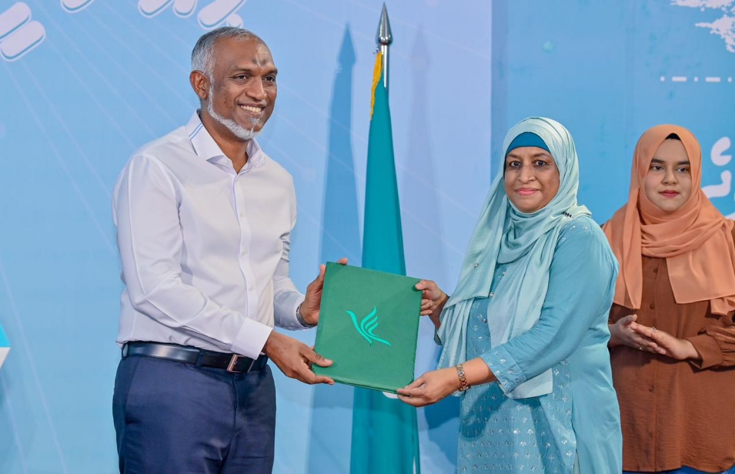 ޕީއެންސީ ހައުސް ހުޅުވަމަށް ބޭއްވި ރަސްމިއްޔާތުގައި އެ ޕާޓީގެ ޖަގަހަ ހުޅުވި ހ. ވެޔޮވިލާ ގޭގެ ވެރިޔާ ޝަފިއްޔާ ޕީއެންސީ އަށް ސޮއިކުރުމަށް ފަހު، އޭނާގެ ފޯމު ރައީސް ޑރ. މުހައްމަދު މުއިއްޒާ ހަވާލު ކުރައްވަނީ.--- ފޮޓޯ: ޕީއެންސީ