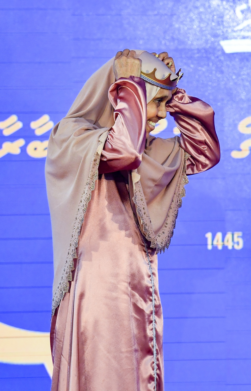 ގައުމީ ގުރުއާން މުބާރާތުގައި ބައިވެރިވި ދުވަސްވީ މީހަކު ތާޖު އަޅައިގެން ސްޓޭޖުން ފައިބަނީ -- ފޮޓޯ: ރައީސް އޮފީސް