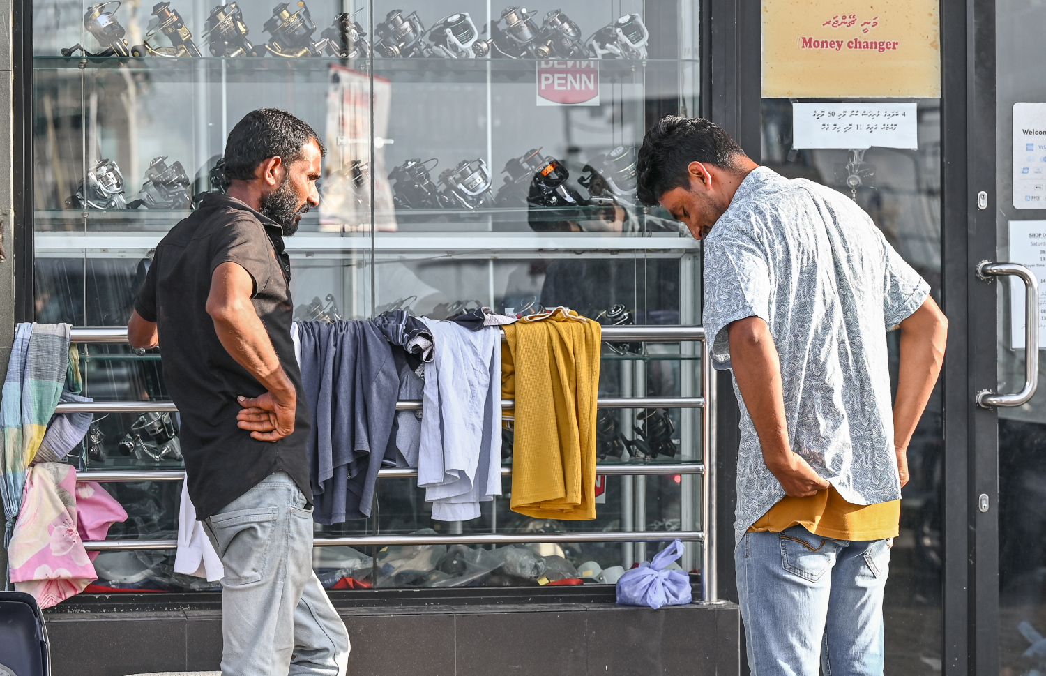 ބާޒާރުމަތީގެ ޕޭވްމަންޓުގައި ހިންގާ 'ކުނިބުނީ' ގެ ފިހާރަކުން މީހަކު ގަމީހެއް ހެޔޮވަރުކުރާއިރު ކައިރީގައި އެހެން މީހަކު ބަލަހައްޓައިގެން. -- ފޮޓޯ: ނިޝާން އަލީ | މިހާރު