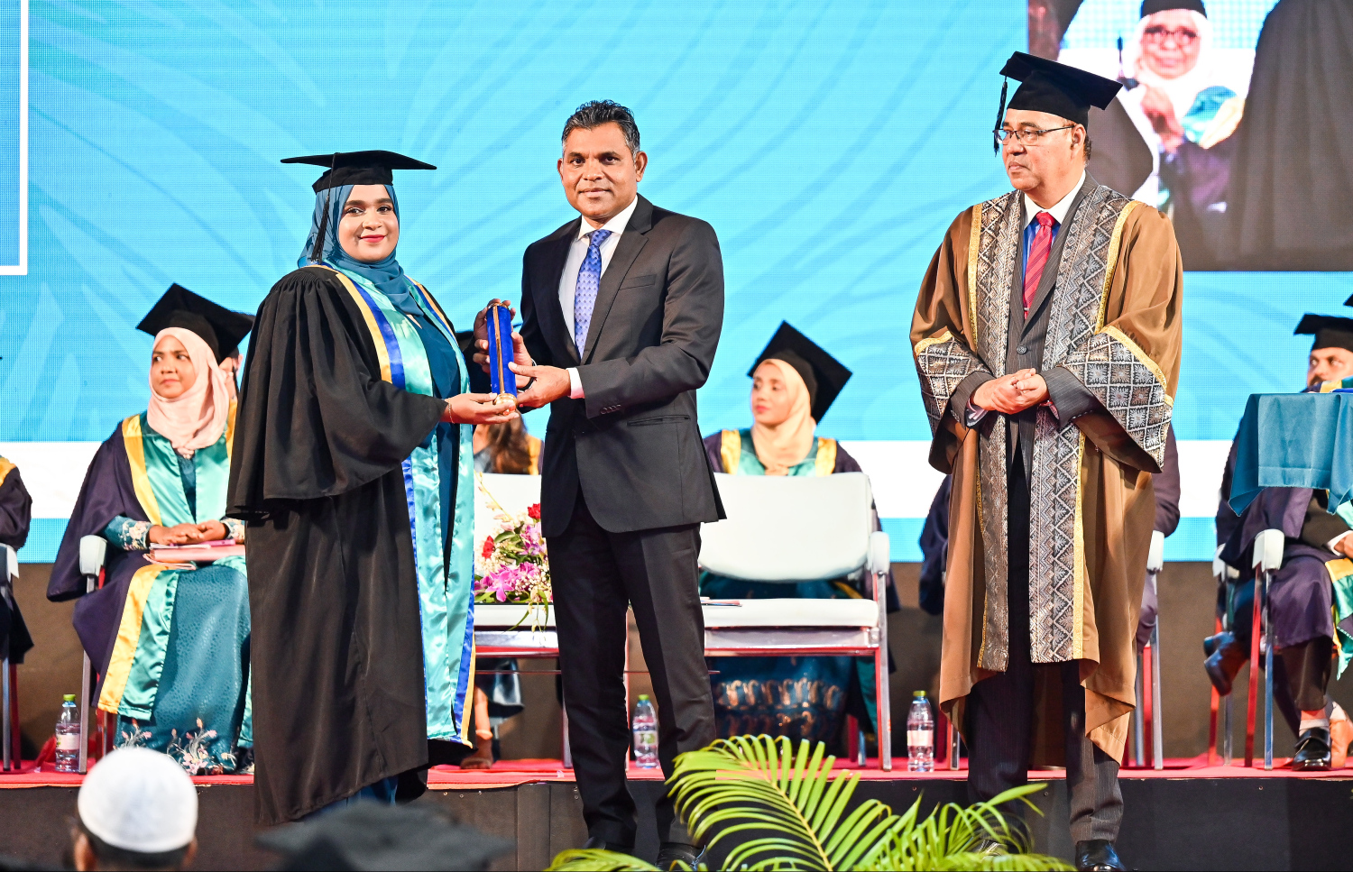 އެމްއައި ކޮލެޖުން މި އަހަރު ގްރެޖުއޭޓްވި ދަރިވަރަކާ ކުރީގެ ނައިބު ރައީސް ފައިސަލް ސެޓްފިކެޓް ހަވާލު ކޮށްދެއްވާއިރު، އަރިހުގައި އެ ކޮލެޖުގެ ޗެއާމަން އަހުމަދު މޮއްޓާކީ.--- ފޮޓޯ: ފަޔާޒު މޫސާ | މިހާރު