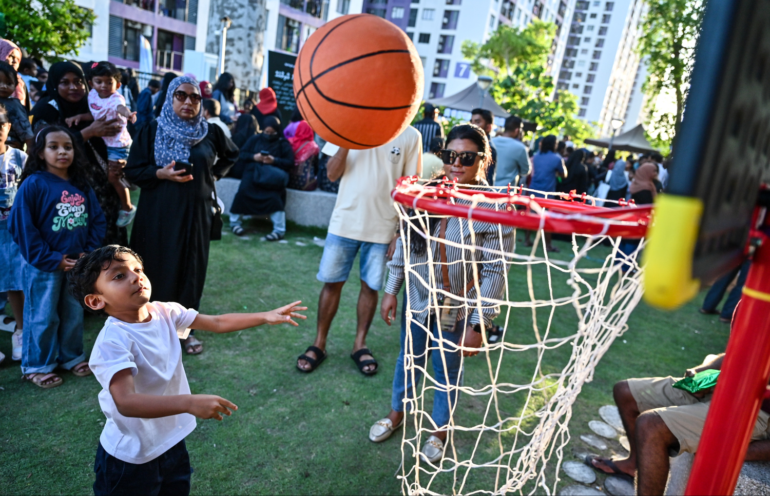 ކުޑަކުދިންގެ ދުވަސް ފާހަގަކުރަން އެޗްޑީސީގެ ފަރާތުން ހިޔާ ޕާކްގައި ބޭއްވި ހަރަކާތުގައި ކުޑަކުއްޖަކު ބާސްކެޓް ބޯޅައެއް އެއްލަނީ. މި ހަވީރުގައި ގިނަ އަދަދެއްގެ ކުދިން ވަނީ ބައިވެރިވެފައި - ފޮޓޯ: ފަޔާޒު މޫސާ | މިހާރު