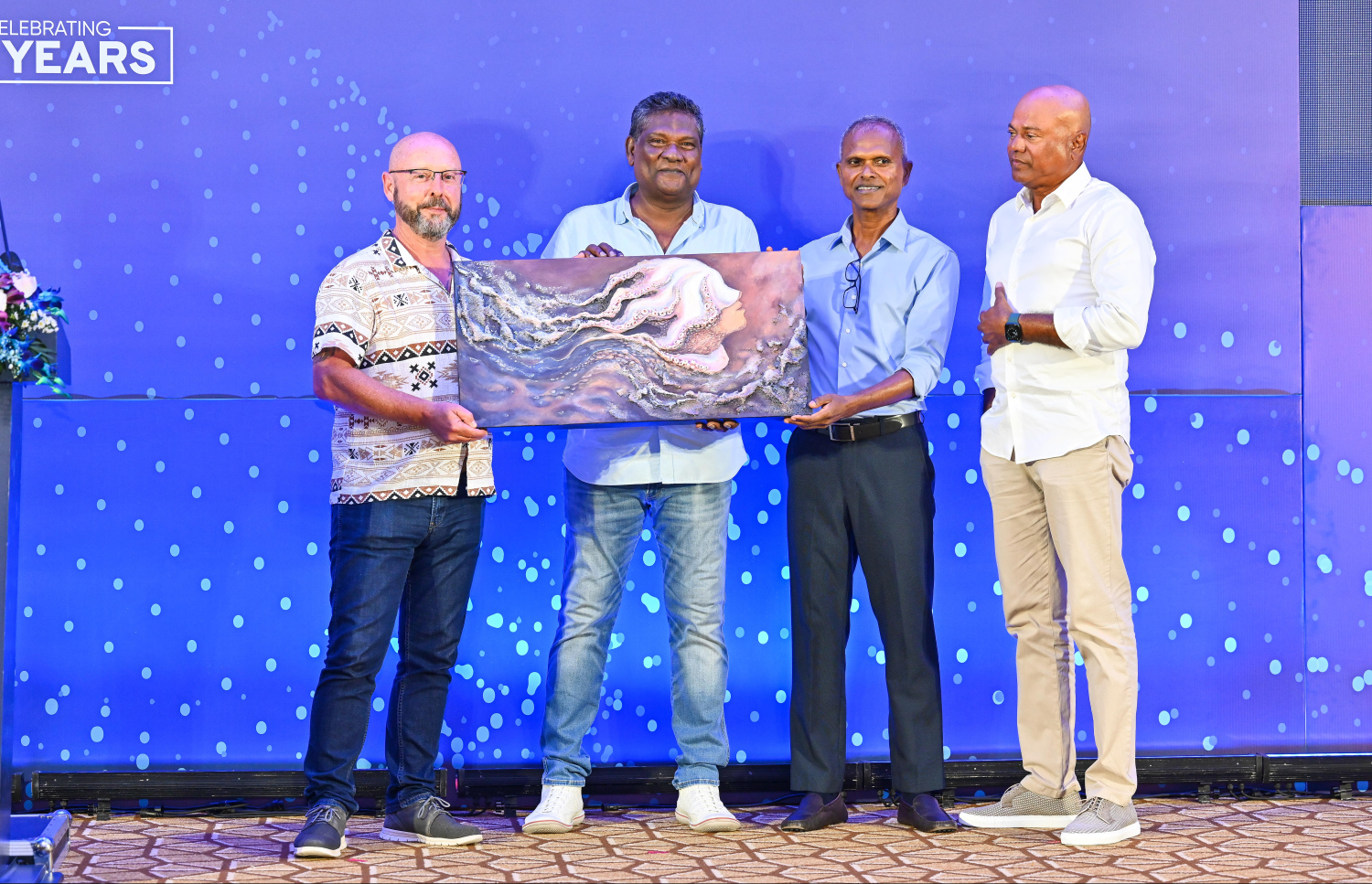 ސިލްވާ ސޭންޑްސް އަށް 25 އަހަރު ފުރުން ފާހަގަކުރުމަށް ބޭއްވި ރަސްމިއްޔާތުގައި، ކުރެހުންތެރިއަކު ތައްޔާރު ކޮށްފައިވާ ކުރެހުމެއް އެ ކުންފުނީގެ އިސްވެރިންނަށް ހަދިޔާ ކުރަނީ.---ފޮޓޯ: ފަޔާޒު މޫސާ| މިހާރު