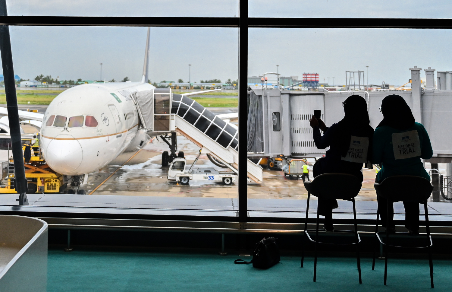 ވެލާނާ އިންޓަނޭޝަނަލް އެއާޕޯޓުގެ އާ ޓާމިނަލް ހުޅުވުމުގެ ކުރިން ކުރިއަށް ގެންދާ ފުލް ޓްރަޔަލްގައި ފުރަން ގޮސް ތިބި ދެ މީހަކު ޓާމިނަލް ބޭރުގައި އޮތް ފްލައިޓެއްގެ ފޮޓޯއެއް ނަގަނީ.--- ފޮޓޯ: ފަޔާޒު މޫސާ | މިހާރު