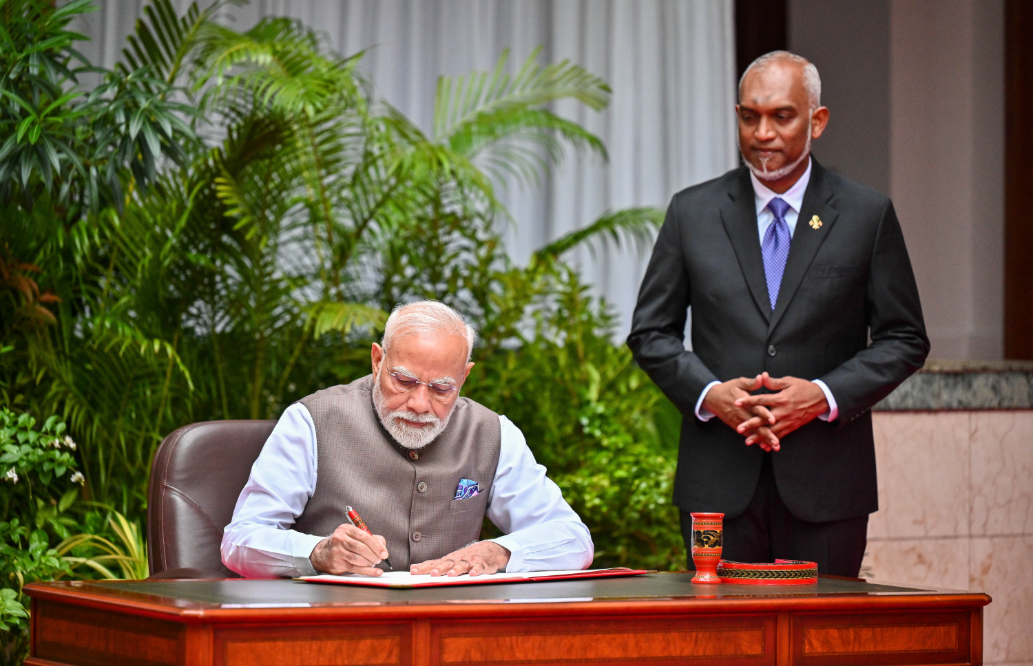 އިންޑިއާގެ ބޮޑުވަޒީރު ނަރެންދުރަ މޯދީ ރައީސް އޮފީހަށް ވަޑައިގެން މެހުމާނުން ސޮއިކުރައްވާ ފޮތުގައި ސޮއިކުރަށްވަނީ އަދި އަރިހުގައި ރައީސް ޑރ މުހައްމަދު މުއިއްޒު.--- ފޮޓޯ: ފަޔާޒު މޫސާ | މިހާރު