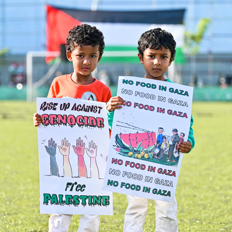 އިޒްރޭލުގެ ޖަރީމާތަކާ ދެކޮޅަށް މާލޭގައި ބޭއްވި ބޮޑު އެއްވުމުގައި ބައިވެރިވި ކުޑަ ދެކުއްޖަކު، ގާޒާގެ ހާލަތު އަންގައިދޭ ޕޯސްޓަރެއ ހިފައިގެން ފޮޓޯއަކަށް ތައްޔާރުވެގެން.--- ފޮޓޯ: ފަޔާޒު މޫސާ | މިހާރު