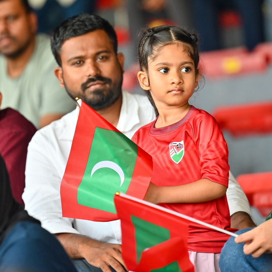 އޭޝިއަން ކަޕް ކޮލިފައިންގައި ރާއްޖެއާ ތަޖިކިސްތާން ބައްދަލުކުރި މެޗު ބަލަން ދަނޑުގައި ހުރި ކުއްޖަކު ގައުމީ ދިދަ ހިފައިގެން ގައުމީ ޓީމަށް ސަޕޯޓްކުރަނީ --- މިހާރު ފޮޓޯ/ފަޔާޒް މޫސާ