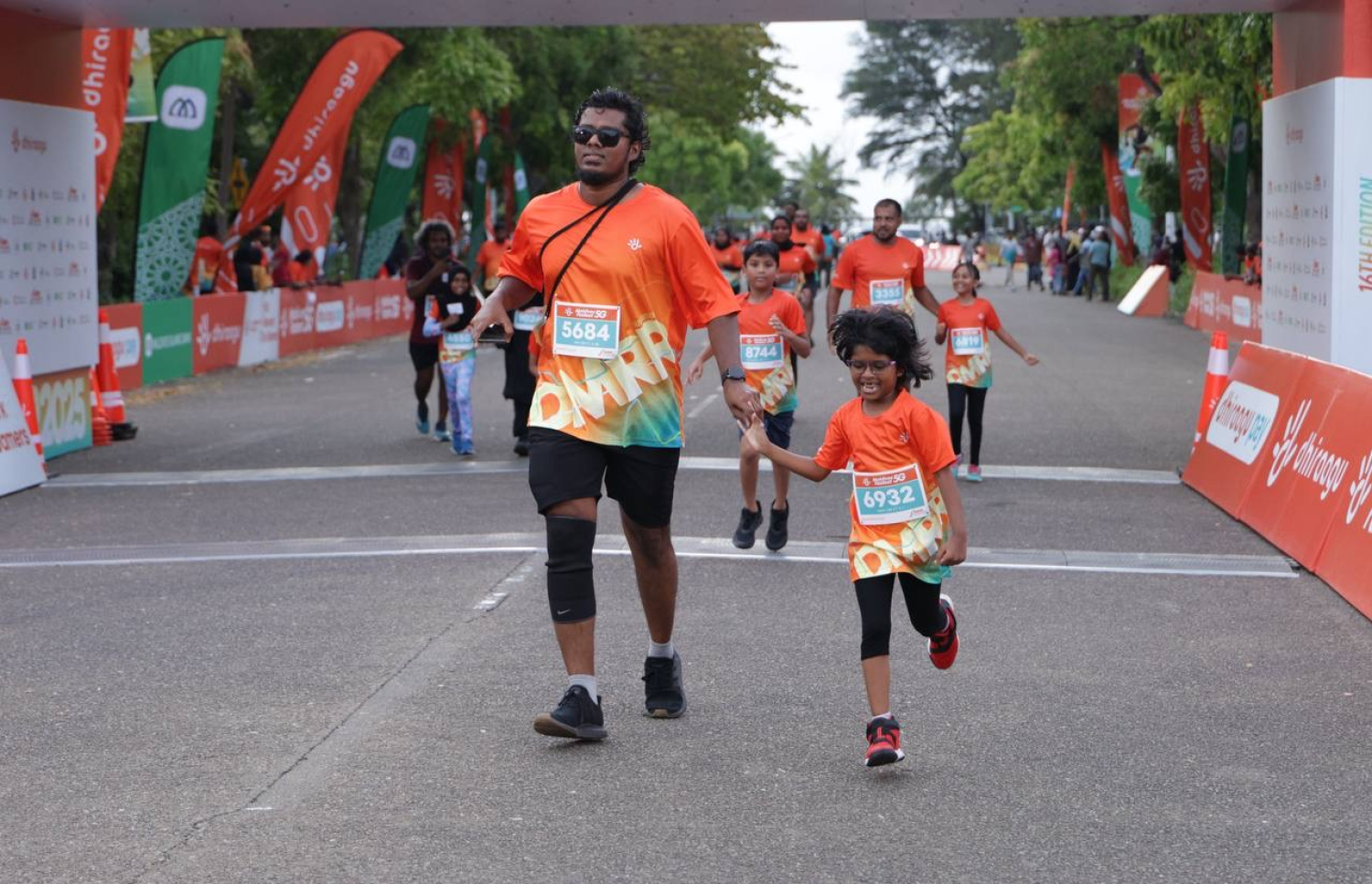 ރާއްޖޭގައި ބާއްވާ ދުވުމުގެ އެންމެ ބޮޑު ރޭސް، ދިރާގު މޯލްޑިވްސް ރޯޑް ރޭހުގައި މީހަކު ކުޑަކުއްޖެއްގެ އަތުގައި ހިފައިގެން ދުވަނީ.--- ފޮޓޯ: ދިރާގު