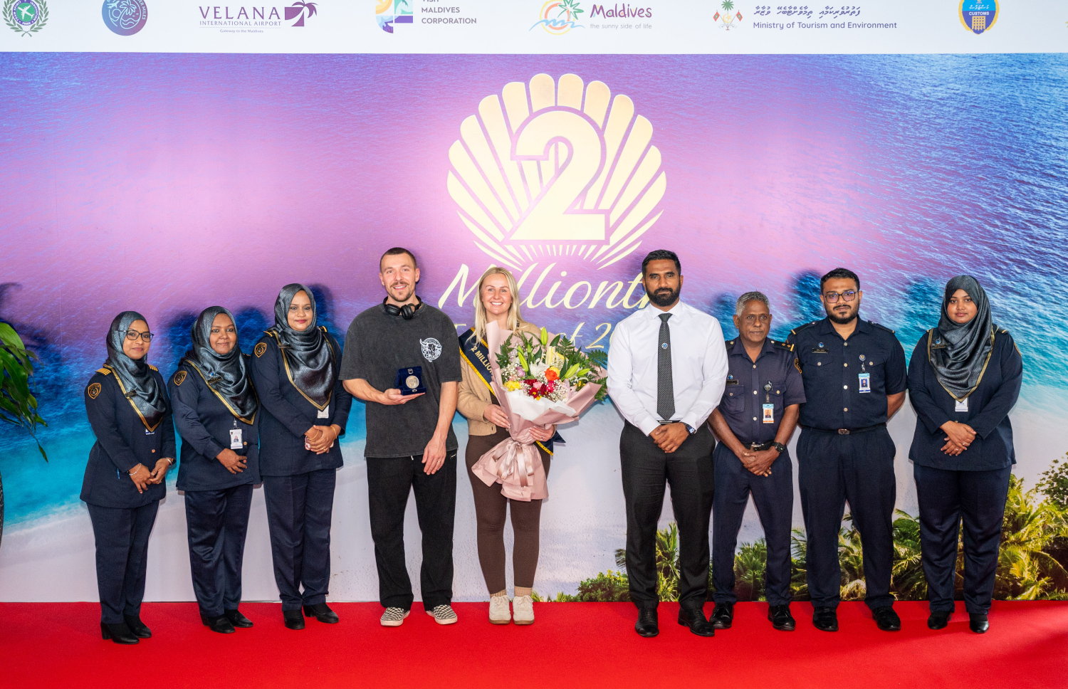 ރާއްޖެ އަށް ޒިޔާރަތްކުރި ދެ މިލިއަން ވަނަ ޓޫރިސްޓުގެ ޝަރަފު ހޯދި އިނގިރޭސި ވިލާތުގެ ބެތަނީ ސާރާ ކާސްވެލްއާ އެކު، އިމިގްރޭޝަން ބައެއް އޮފިސަރުން ފޮޓޯއެއް ނަގަނީ.---ފޮޓޯ: ނިޝާން އަލީ| މިހާރު