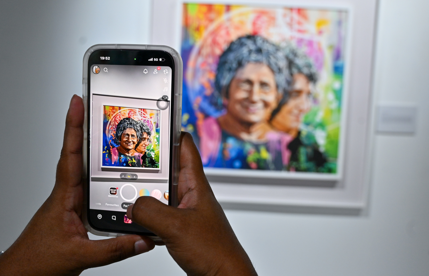 "ވިވިޑް ރިއަލިޒަމް - ބައި ހުސައިން" އާޓް އެގްޒިބިޝަން ޒިޔާރަތްކުރި މީހަކު ފޯނުން ކުރެހުންތެރިޔާ ހުސައިން އަލީ މަނިކުގެ ކުރެހުމެއްގެ ފޮޓޯއެއް ނަގަނީ.-- ފޮޓޯ: ފަޔާޒު މޫސާ | މިހާރު