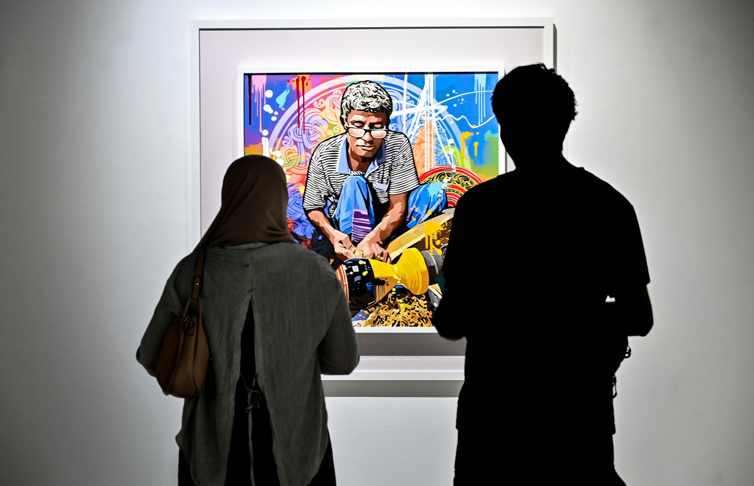 "ވިވިޑް ރިއަލިޒަމް - ބައި ހުސައިން" އާޓް އެގްޒިބިޝަނަށް ޒިޔާރަތްކުރި މީހަކު ކުރެހުންތެރިޔާ ހުސައިން އަލީ މަނިކުގެ ކުރެހުންތައް ބަލަނީ.-- ފޮޓޯ: ފަޔާޒު މޫސާ | މިހާރު