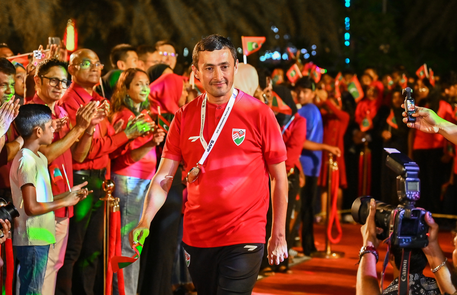 ފުޓްސަލް ޗެމްޕިއަންކަން ހޯދި ރާއްޖޭގެ ގައުމީ ފުޓްސަލް ޓީމުގެ ކޯޗު ފަރުރޫކް ޒަކިރޯވްއަށް ސަޕޯޓަރުން މަރުހަބާ ކިޔަނީ.-- ފޮޓޯ: ފަޔާޒު މޫސާ | މިހާރު