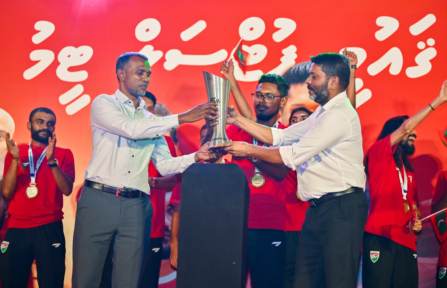 ފުރަތަމަ ފަހަރަށް ބޭއްވި ސާފް ފުޓްސަލް މުބާރާތުގެ ތަށި ހުރިހާ މެޗަކުން މޮޅުވެ ހޯދި ރާއްޖޭގެ ގައުމީ ފުޓްސަލް ޓީމު ރާއްޖެ އައުމުން މަރުހަބާ ކިޔުމަށް ބޭއްވި އިވެންޓުގައި ޓީމުގެ ފަރާތުން އެފްއޭއެމްގެ ރައީސް އަހުމަދު ތޯރިގް އާއި ސްޕޯޓްސް މިނިސްޓަރު އަބްދުﷲ ރާފިއުއަށް ތަށި ހަވާލުކުރަނީ.-- ފޮޓޯ: ފަޔާޒު މޫސާ | މިހާރު