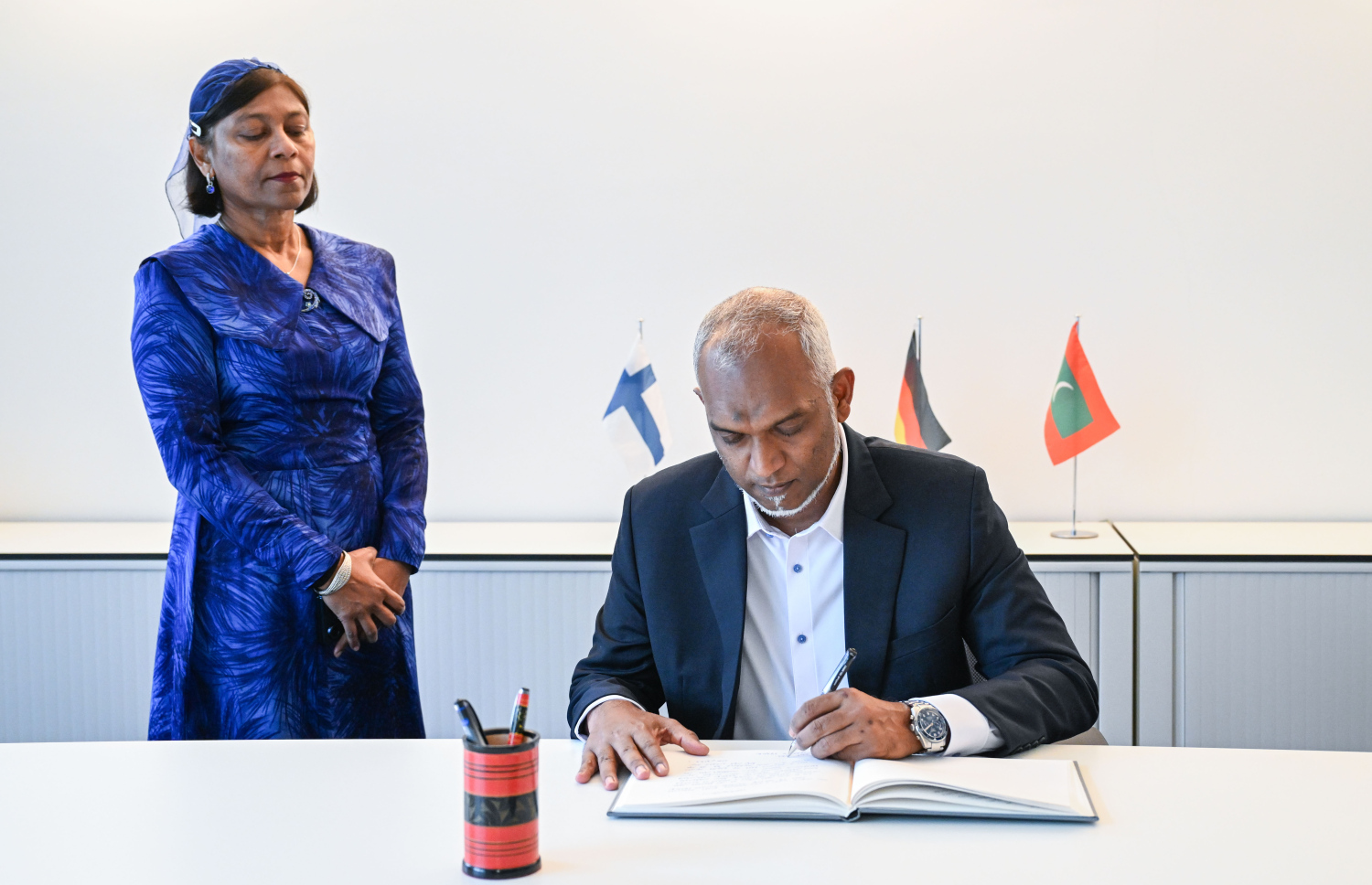 ރައީސް މުއިއްޒު ޖަރުމަނަށް މިހާރު ކުރައްވަމުން ގެންދަވާ ރަސްމީ ދަތުރުފުޅުގައި ރާއްޖޭގެ އެމްބަސީއަށް ކުރެއްވި ޒިޔާރަތުގައި މެހުމާނުން ލިޔުއްވާ ފޮތުގައި ރައީސް ލިޔުއްވަނީ -- ފޮޓޯ: ރައީސް އޮފީސް