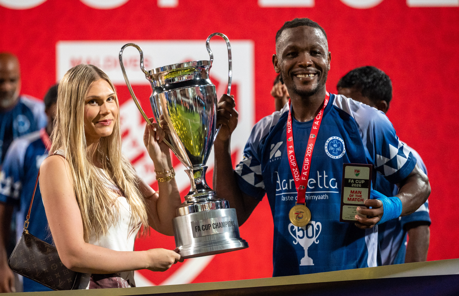 ފައިނަލުގައި ޓީސީ ސްޕޯޓްސް ބަލިކޮށް އެފްއޭ ކަޕް ކާމިޔާބުކުރި ނިއު ރޭޑިއަންޓުގެ ބޭރު ކުޅުންތެރިޔާ ނައިޖީރިއާގެ ފޯވާޑް އަލްހާޖީ ޖެރޯ އޭނާގެ އާއިލާއާ އެކު ތައްޓާ އެކު ފޮޓޯއެއް ނަގަނީ.-- ފޮޓޯ: ފަޔާޒު މޫސާ | މިހާރު