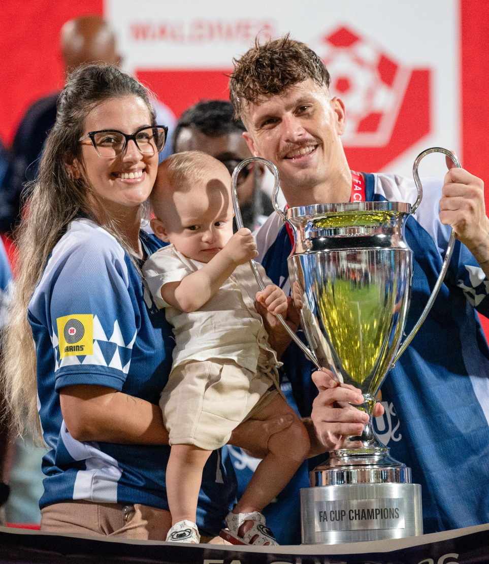 ފައިނަލުގައި ޓީސީ ސްޕޯޓްސްގެ މައްޗަށް 3-0 ގެ ނަތީޖާއަކުން ކާމިޔާބު ހޯދައި، އެފްއޭ ކަޕްގެ ޗެމްޕިއަންކަން ހޯދި ނިއު ރޭޑިއަންޓުގެ ބޭރު ކުޅުންތެރިޔާ ލޫއިސް ގޯމެސް ޑާ ސިލްވާ އޭނާގެ އާއިލާއާ އެކު ތައްޓާ އެކު ފޮޓޯއެއް ނަގަނީ.-- ފޮޓޯ: ފަޔާޒު މޫސާ | މިހާރު