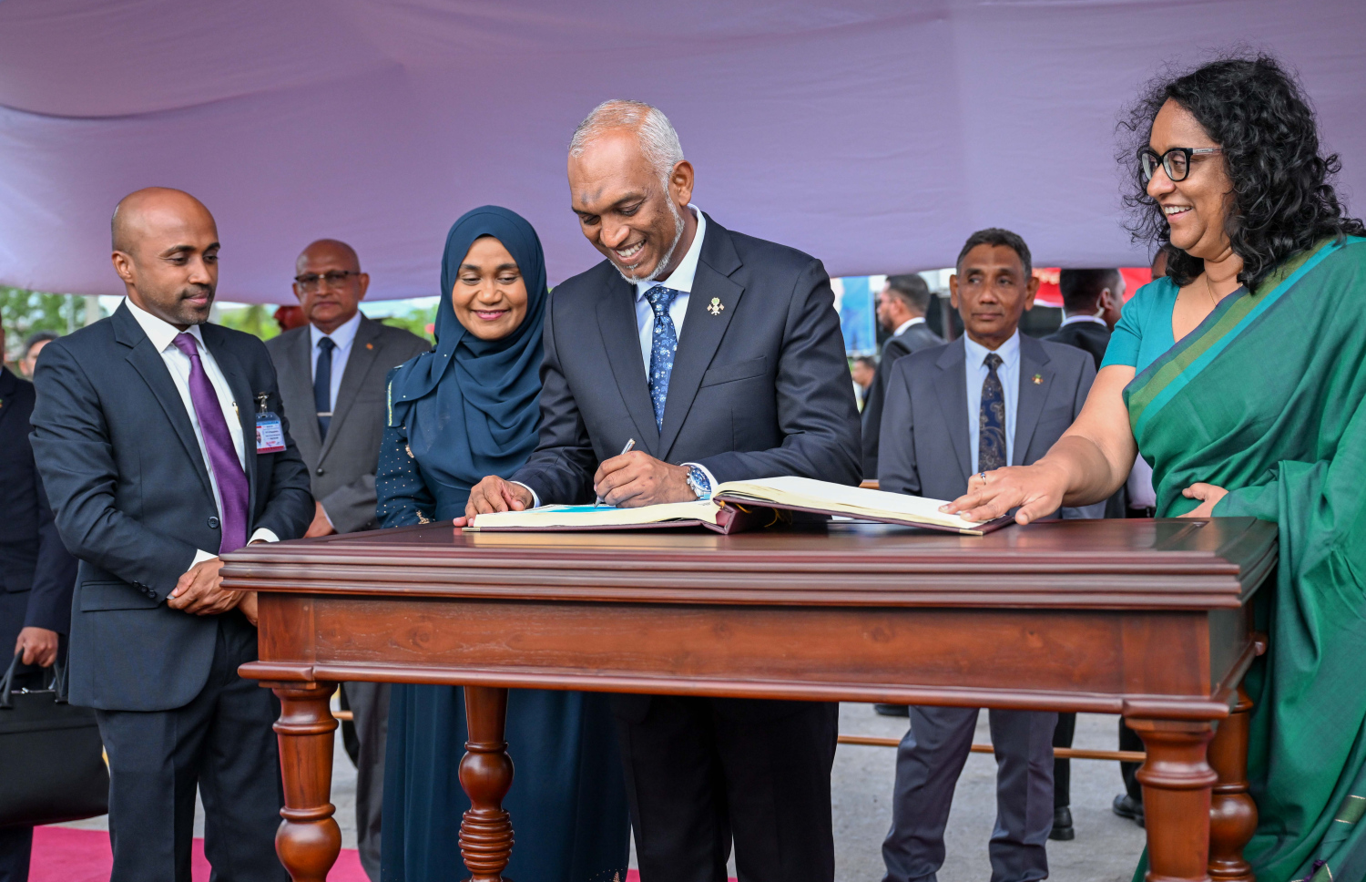 ރައީސް ޑރ. މުހައްމަދު މުއިއްޒުގެ ދެކަނބަލުން ލަންކާއަށް ކުރައްްވަމުން ގެންދަވާ ދަތުރުފުޅުގައި، ލަންކާ އެއާޕޯޓުގައި މެހުމާނުން ސޮއި ކުރާ ފޮތުގައި ސޮއިކުރައްވަނީ -- ފޮޓޯ: ރައީސް އޮފީސް