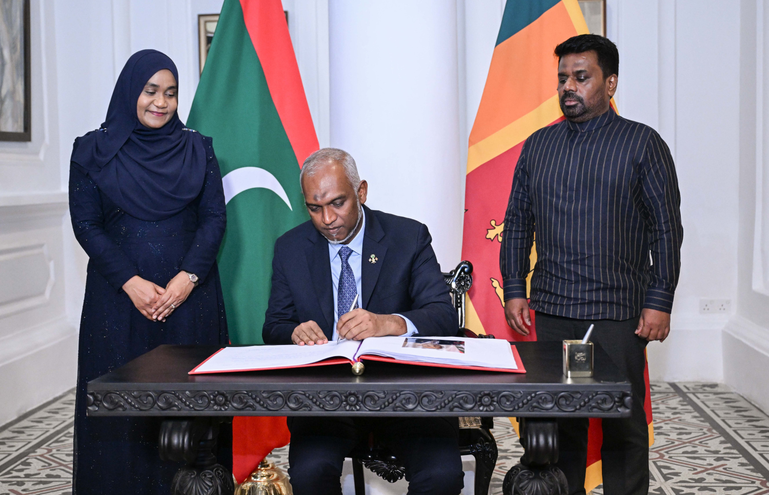 ރައީސް ޑރ މުހައްމަދު މުއިއްޒުގެ ދެކަނބަލުންގެ ޝަރަފުގައި ސްރީލަންކާގެ ރައީސް އަނޫރާ ކުމާރާ ޑިސަނާޔަކެ ދެއްވި ރަސްމީ ޖާފަތުގައި ބައިވެރިވެ ވަޑައިގެން މެހުމާނުން ސޮއިކުރައްވާ ފޮތުގައި ރައީސް ސޮއި ކުރައްވަނީ -- ފޮޓޯ؛ ރައީސް އޮފީސް