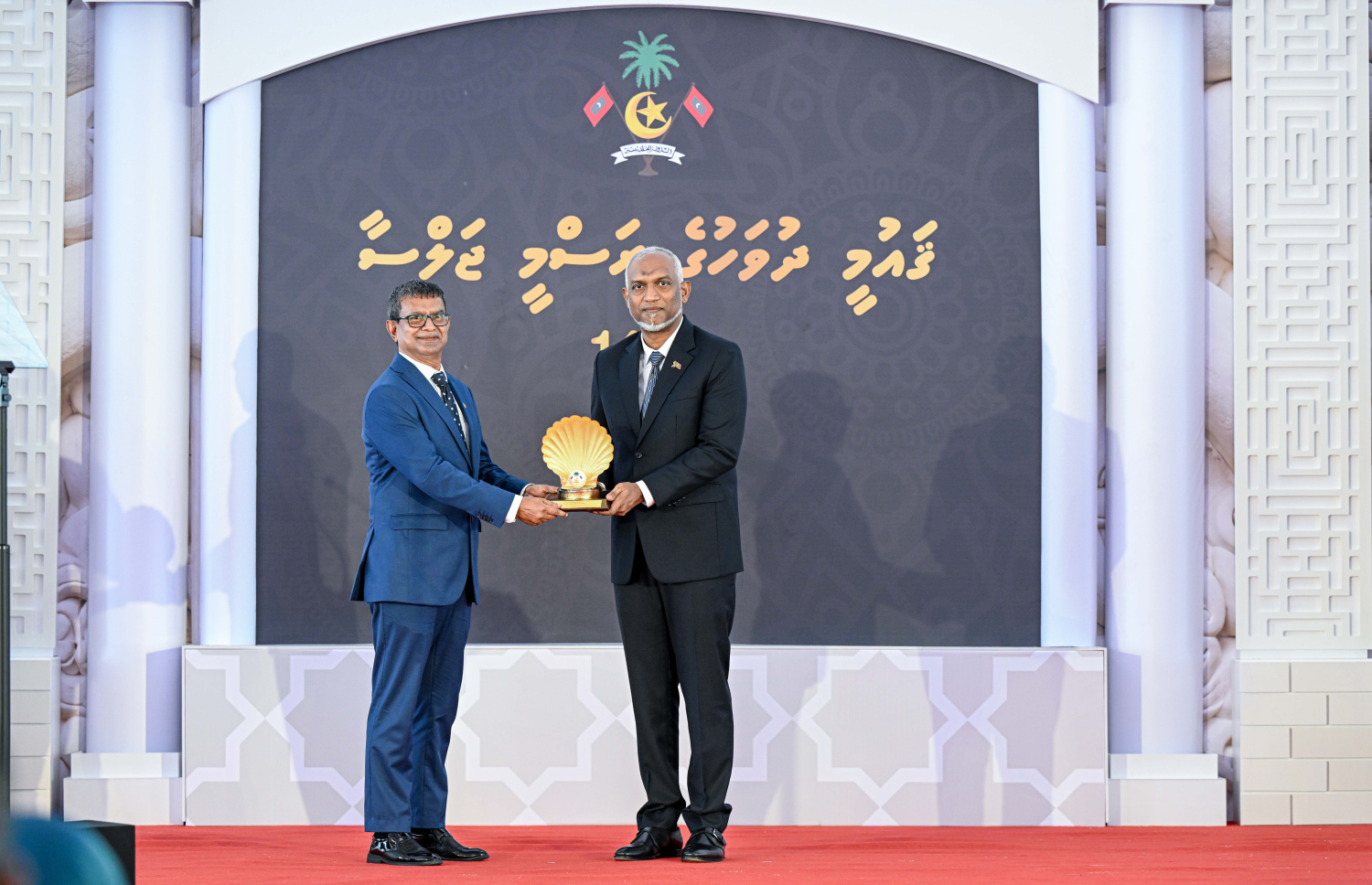 ދިވެހި އަދަބިއްޔާތުގެ ދާއިރާއިން ޝަރަފުވެރިކަމުގެ ގައުމީ އިނާމު ލިބިވަޑައިގެންނެވި އަހުމަދު އާމިރު (ފަރެސް އާމިރު)އަށް ރައީސް ޑރ. މުހައްމަދު މުއިއްޒު އިނާމު ހަވާލުކޮށް ދެއްވަނީ.-- ފޮޓޯ: ރައީސް އޮފީސް